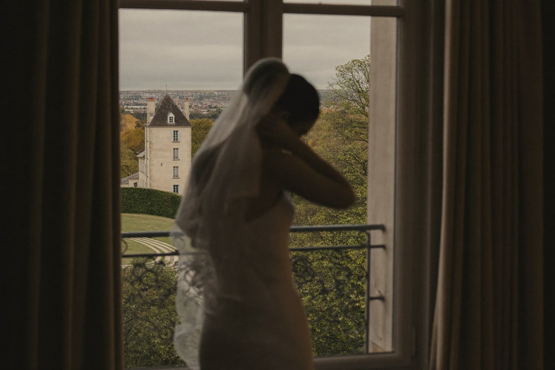 Bride adjusting her veil by a château window — wedding film by Basil Studios